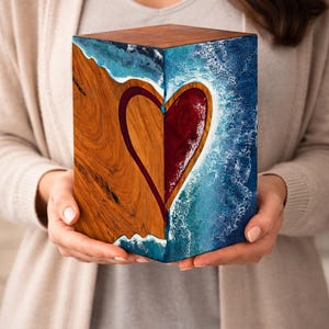May include: A wooden cube with a heart design. One side features a wood grain pattern, the other a blue and white ocean-like design. The heart is divided, with one half in wood and the other in red.