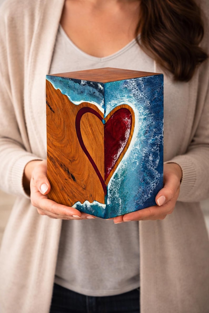 May include: A wooden cube with a heart design. One side features a wood grain pattern, the other a blue and white ocean-like design. The heart is divided, with one half in wood and the other in red.