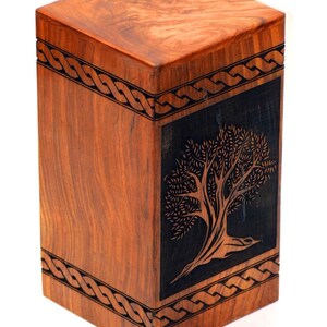 May include: A wooden cremation urn with a Celtic knot design and a carved tree on the front. The urn is made of dark wood with a natural finish.