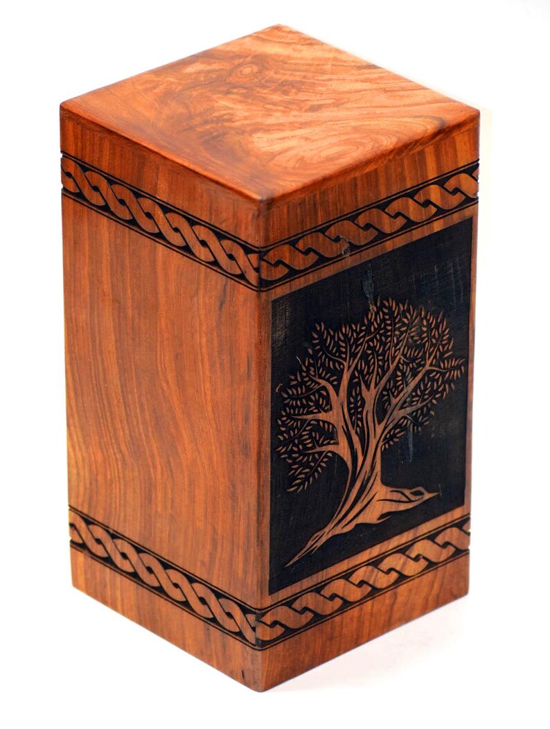 May include: A wooden cremation urn with a Celtic knot design and a carved tree on the front. The urn is made of dark wood with a natural finish.