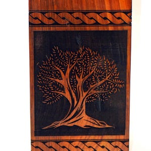 May include: A wooden box with a dark brown finish and a carved tree design on the front. The box has a Celtic knot border around the top and bottom.