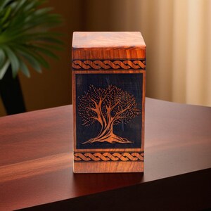 May include: A wooden box with a dark brown finish and a carved tree design. The box has a Celtic knot border around the tree design.