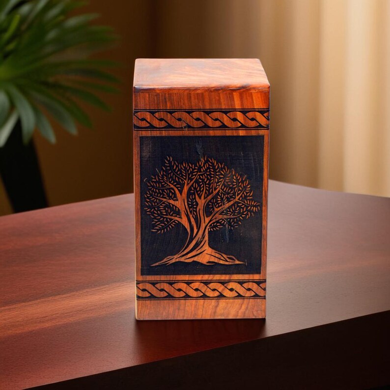 May include: A wooden box with a dark brown finish and a carved tree design. The box has a Celtic knot border around the tree design.