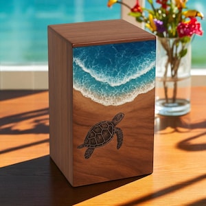 May include: A wooden box with a detailed ocean scene and a sea turtle design. The top of the box features a blue ocean with white waves, transitioning to a sandy beach. A sea turtle is depicted on the front of the box.