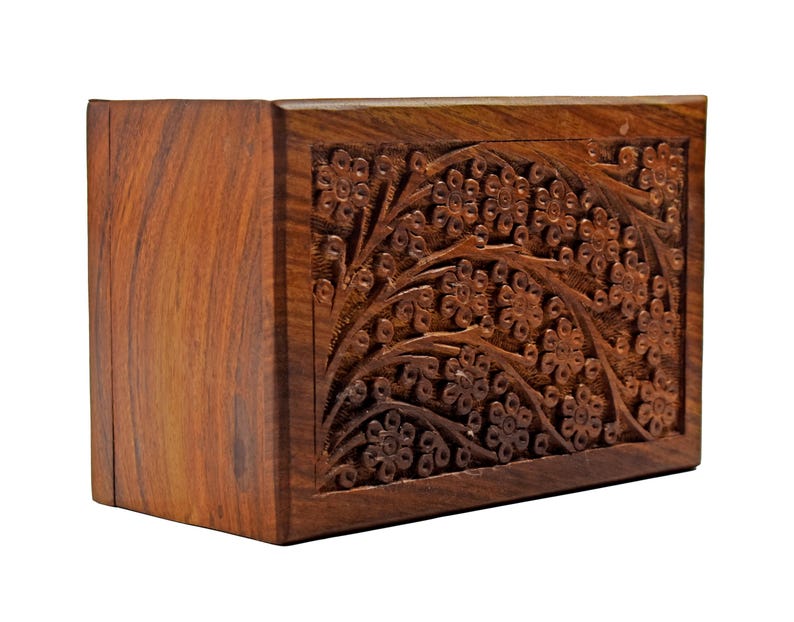 Puede incluir: Una peque&ntilde;a caja de madera con un dise&ntilde;o floral tallado. La caja est&aacute; hecha de madera marr&oacute;n oscura y tiene una forma rectangular.
