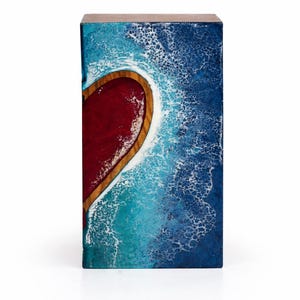 May include: A rectangular wooden box with a heart-shaped design. The heart is filled with red resin and framed by a wooden border. The background features a blue and white wave pattern, creating a coastal theme.