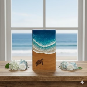 Pode incluir: Uma peça de arte retangular em madeira com uma cena de praia. A parte superior mostra um oceano azul vibrante com ondas brancas, que leva a uma praia arenosa na parte inferior. Uma tartaruga marinha castanha está gravada na praia. A peça é exibida em uma mesa de madeira.