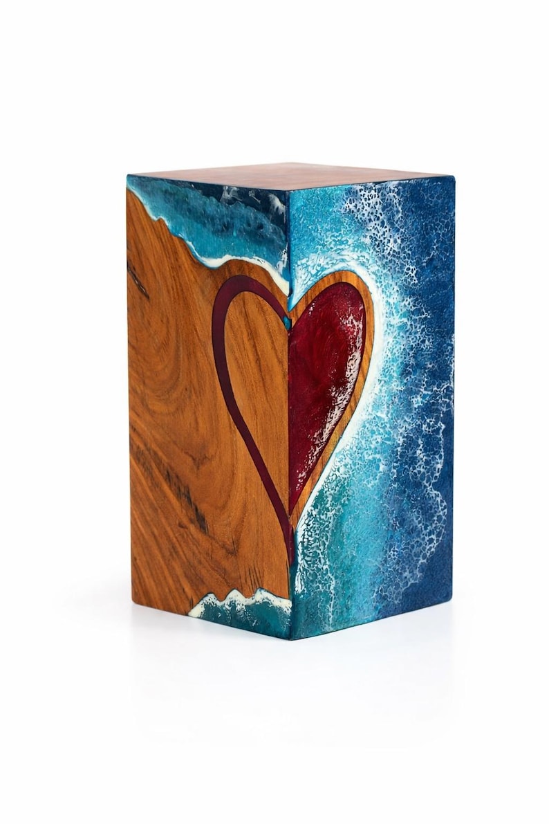 May include: A wooden block with a heart design. One side features natural wood grain, the other a blue and white ocean-like resin. The heart is red with a dark purple outline. The top is a dark brown color.
