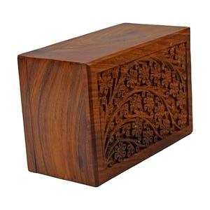 Puede incluir: Una caja de madera marr&oacute;n oscuro con intrincados tallados florales en la parte delantera. La caja tiene un acabado liso y pulido.