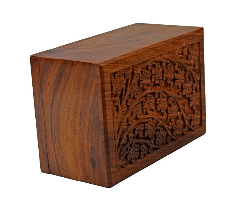 Puede incluir: Una caja de madera marr&oacute;n oscuro con intrincados tallados florales en la parte delantera. La caja tiene un acabado liso y pulido.