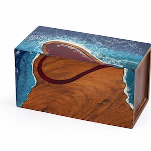 May include: A rectangular wooden box with a heart-shaped design. The top and sides feature a blue and white wave pattern, while the front displays a heart-shaped design in red. The box is made of wood with a natural grain.