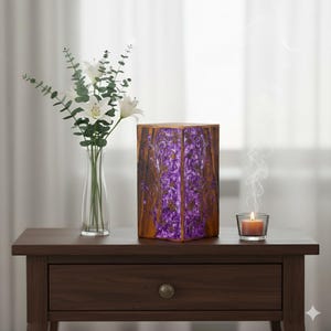 May include: A wooden urn with a purple floral design. The urn is hexagonal and sits on a dark brown nightstand. A vase of white flowers and a lit candle are also on the nightstand.