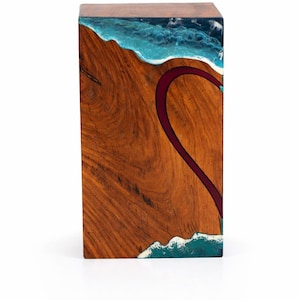 May include: A rectangular wooden side table with a unique design. The top features a blue and white resin wave pattern. The front has a dark red river-like design. The table is made of wood and resin.