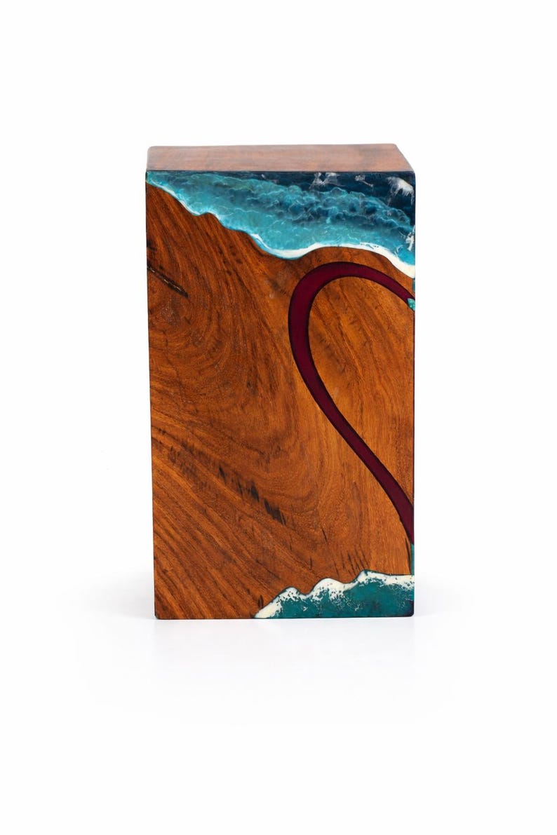 May include: A rectangular wooden side table with a unique design. The top features a blue and white resin wave pattern. The front has a dark red river-like design. The table is made of wood and resin.