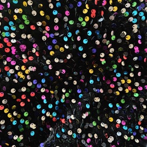 May include: A black fabric surface densely covered with small, round, reflective sequins in a vibrant rainbow of colors including red, yellow, blue, green, and pink. The sequins are arranged in a scattered pattern across the dark background.