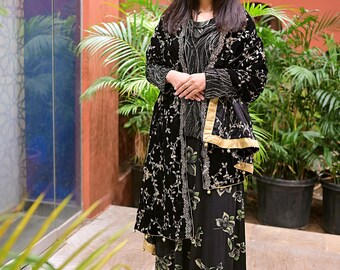 May include: A woman wearing a black velvet shawl with gold embroidery and a black floral print dress. The shawl has a gold trim and pearl accents.