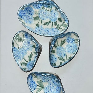 May include: Four blue and white seashells with a floral pattern. The shells are painted with a metallic blue finish.