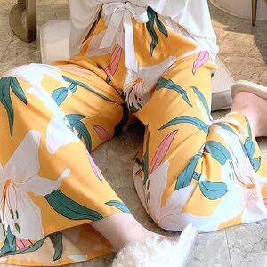 May include: Yellow wide-leg trousers with a white floral print. The trousers have a tie at the waist and are made of a soft, flowing fabric.