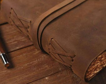 May include: A brown leather-bound journal with a braided leather closure. The journal is closed and lying on a wooden surface.