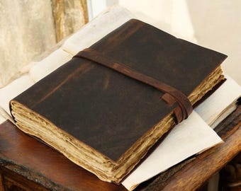 May include: A brown leather-bound journal with a worn, vintage look. The journal has a leather strap closure and is closed, resting on a wooden surface.