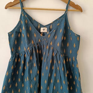 Può includere: Un top blu turchese senza maniche con scollo a V e stampa a foglie dorate. Il top ha un orlo arricciato ed è realizzato in un tessuto leggero. L'etichetta sul top recita "SUKARI".