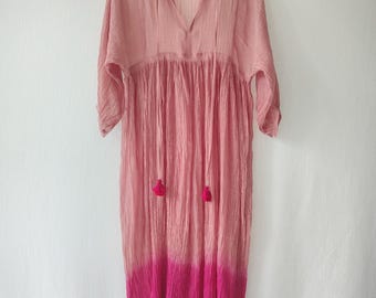 Puede incluir: Un vestido largo y fluido en tonos rosas, con cuello en V y mangas largas. El vestido presenta una cintura fruncida y un vibrante efecto degradado fucsia en el dobladillo. Dos pequeñas borlas cuelgan del escote.