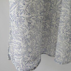 Puede incluir: Primer plano de una tela blanca con un patr&oacute;n floral azul repetido. El dise&ntilde;o presenta flores, hojas y enredaderas estilizadas. La tela parece estar drapeada, con pliegues y curvas suaves.