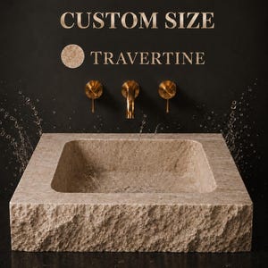 May include: A square beige travertine stone sink with a rough, chiseled exterior texture and a smooth interior basin. Above the sink, three gold-toned wall-mounted faucets are installed. Text reads CUSTOM SIZE TRAVERTINE with a circular sample.