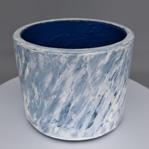May include: A cylindrical ceramic planter with a blue interior and a textured exterior. The exterior features a marbled pattern of light blue and white brushstrokes, creating a unique decorative piece.