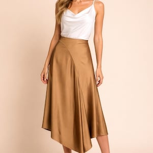 May include: A woman wearing a white cowl neck top and a gold-colored midi skirt. The skirt has an asymmetrical hemline. The woman is also wearing gold-colored high-heeled sandals.