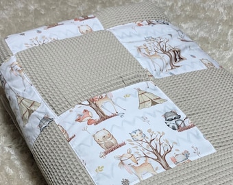 Op de afbeelding: Beige babydeken met wafelweefsel en patches met bosdieren. De patches tonen herten, beren, vossen, wasberen en tipi's. De deken heeft een zachte, neutrale kleur, perfect voor een kinderkamer.