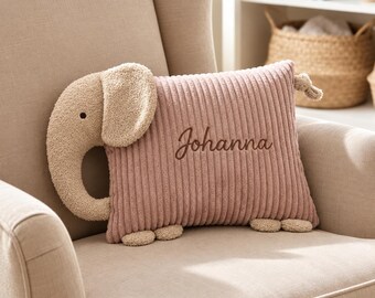 May include: A rectangular dusty pink corduroy pillow shaped like an elephant. The pillow features a textured beige plush elephant head with a trunk and ear on the left side, small beige feet at the bottom, and the name Johanna embroidered in brown.