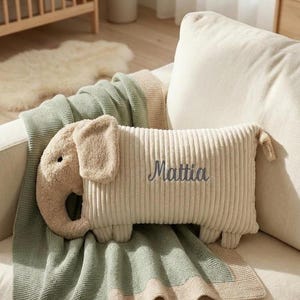 Peut inclure: Un coussin rectangulaire en velours c&ocirc;tel&eacute; beige en forme d'&eacute;l&eacute;phant avec une trompe, des oreilles et quatre petites pattes. Le coussin porte le pr&eacute;nom Mattia brod&eacute; en &eacute;criture cursive gris fonc&eacute; sur le c&ocirc;t&eacute;. La texture est c&ocirc;tel&eacute;e et douce.