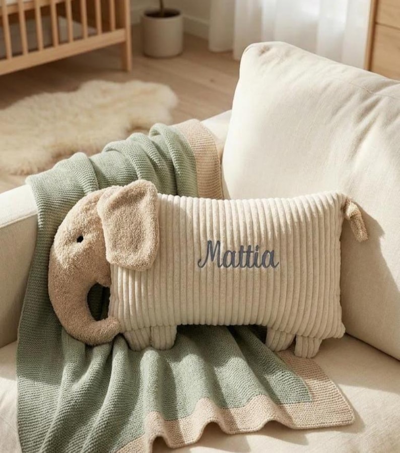 Peut inclure: Un coussin rectangulaire en velours c&ocirc;tel&eacute; beige en forme d'&eacute;l&eacute;phant avec une trompe, des oreilles et quatre petites pattes. Le coussin porte le pr&eacute;nom Mattia brod&eacute; en &eacute;criture cursive gris fonc&eacute; sur le c&ocirc;t&eacute;. La texture est c&ocirc;tel&eacute;e et douce.