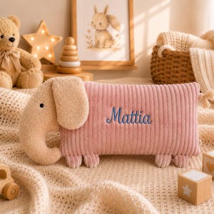 Peut inclure: Un coussin en peluche rectangulaire en forme d'&eacute;l&eacute;phant avec un corps en velours c&ocirc;tel&eacute; rose et une t&ecirc;te textur&eacute;e beige. Le pr&eacute;nom Mattia est brod&eacute; en &eacute;criture bleue sur le c&ocirc;t&eacute; du coussin. L'&eacute;l&eacute;phant a de petites oreilles, une trompe et quatre pieds.