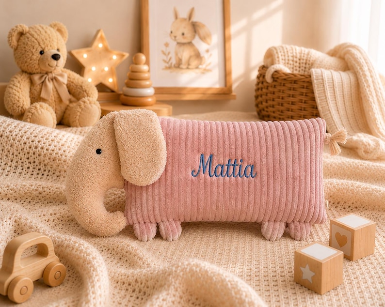 Peut inclure: Un coussin en peluche rectangulaire en forme d'&eacute;l&eacute;phant avec un corps en velours c&ocirc;tel&eacute; rose et une t&ecirc;te textur&eacute;e beige. Le pr&eacute;nom Mattia est brod&eacute; en &eacute;criture bleue sur le c&ocirc;t&eacute; du coussin. L'&eacute;l&eacute;phant a de petites oreilles, une trompe et quatre pieds.