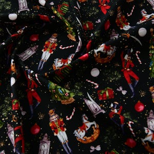 May include: Black fabric featuring a Christmas-themed pattern. The design includes nutcrackers in red and gold uniforms, toy horses, clocks, Christmas trees, candy canes, and baubles. Ideal for festive crafts and sewing projects.