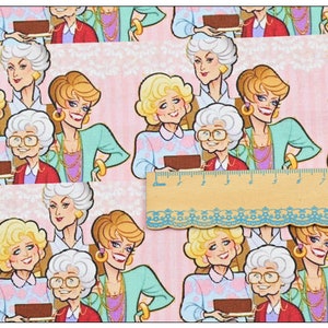 May include: A pink fabric with a repeating pattern of four women. The women are cartoon-like and have blonde hair. They are wearing colorful clothing and holding a tray with a brown cake on it.