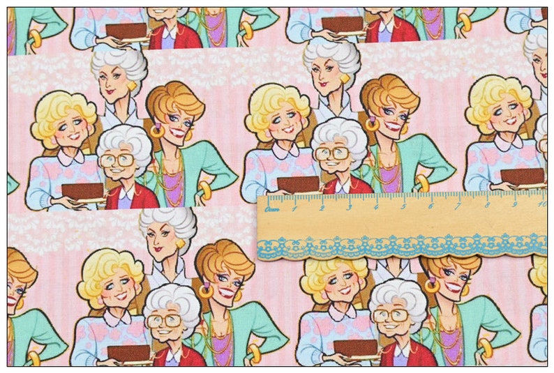 May include: A pink fabric with a repeating pattern of four women. The women are cartoon-like and have blonde hair. They are wearing colorful clothing and holding a tray with a brown cake on it.