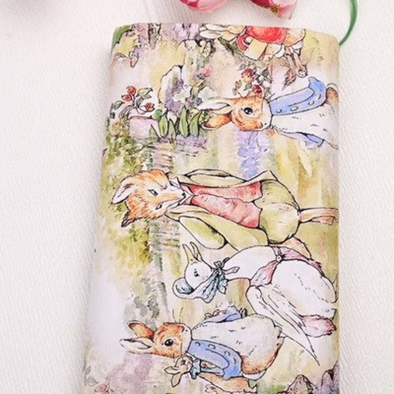 May include: A white fabric with a colorful illustration of Peter Rabbit and friends. The illustration features a fox, a rabbit, a duck, and a goose. The fabric is perfect for crafting projects, such as quilting, sewing, and scrapbooking.