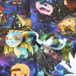 May include: Fabric featuring a colorful galaxy design with cartoon dragons and characters. The fabric has a dark blue background with illustrations of dragons, Vikings, and other fantasy elements. The dragons are in shades of blue, white, and black.