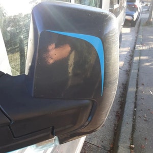 Puede incluir: Un espejo retrovisor lateral negro con una franja de acento azul. El espejo está unido a un vehículo.