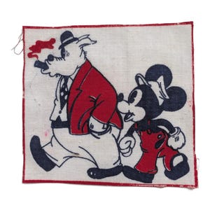 Op de afbeelding: Een vierkante stoffen patch met een gedrukte illustratie van een getekend varken in een rood jasje en zwarte hoed dat een sigaar rookt, lopend naast een getekende muis in een rode tuinbroek en witte pet, omrand door een dunne rode lijn.