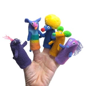 Peut inclure: Un ensemble de cinq marionnettes à doigt en feutrine colorée avec des yeux mobiles. Les marionnettes comprennent une violette avec des cheveux roses, une bleue rayée arc-en-ciel, une bleu foncé avec un pompon jaune, une orange et une violette à franges.