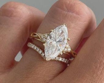May include: A marquise-cut diamond engagement ring with a gold band, accompanied by a curved diamond wedding band. The rings feature small, sparkling stones, creating a brilliant display. The bands are a warm gold colour, showcasing a classic design.