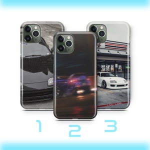 Puede incluir: Tres fundas de teléfono diferentes con imágenes de coches. La primera funda presenta un coche negro con un fondo borroso. La segunda funda presenta una imagen borrosa de un coche azul con luces rojas y amarillas. La tercera funda presenta un coche blanco aparcado delante de una tienda con un toldo rojo y blanco a rayas.