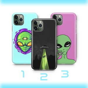 Op de afbeelding: Drie verschillende telefoonhoesjes met alien-ontwerpen. De eerste hoes is lichtblauw met een groene alien met een derde oog. De tweede hoes is zwart met een groene alien-spaceship en een groene lichtstraal. De derde hoes is roze met een groene alien die een joint rookt.