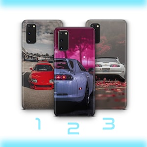 Puede incluir: Tres fundas para teléfono con diferentes imágenes de un coche deportivo Toyota Supra blanco y rojo. La primera funda tiene un fondo gris con un Supra rojo en primer plano. La segunda funda tiene un fondo rosa y morado con un Supra blanco en primer plano. La tercera funda tiene un fondo gris con un Supra blanco en primer plano.