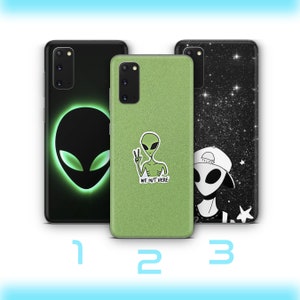 Può includere: Tre diverse custodie per telefono con disegni di alieni. La prima custodia ha una testa di alieno verde con occhi luminosi su uno sfondo nero. La seconda custodia ha un alieno verde con un segno di pace su uno sfondo di glitter verde. La terza custodia ha un alieno bianco e nero con un cappello su uno sfondo nero con stelle bianche.