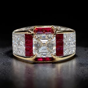 May include: A gold ring featuring a large square-cut centre diamond surrounded by a frame of vibrant red square-cut rubies. The band is encrusted with multiple rows of small, clear square-cut diamonds, creating a wide, ornate, and symmetrical design.